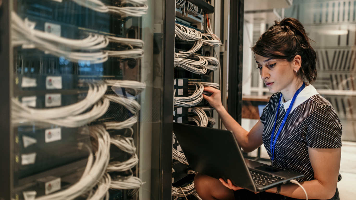 image shows a woman in a server room adjusting network settings while looking at her laptop